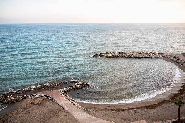 Serene coastal scene features gentle waves lapping against rocky shoreline at sunset