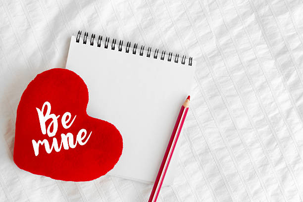 istock Heart-shaped pillow with message and blank notebook on a white bedspread 2246148697