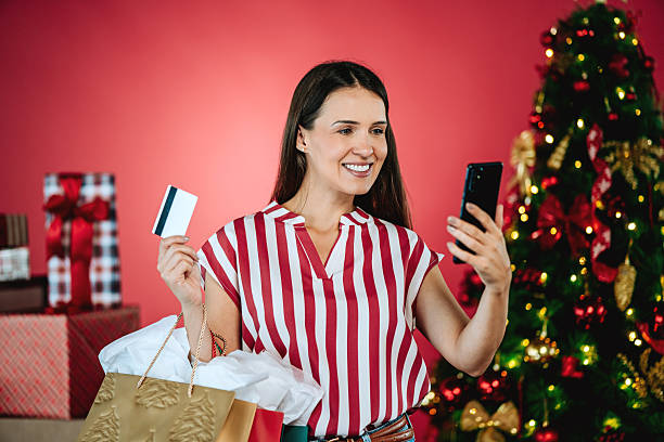 istock Smiling woman looking at camera while holding credit card and smartphone in Christmas studio 2246152603
