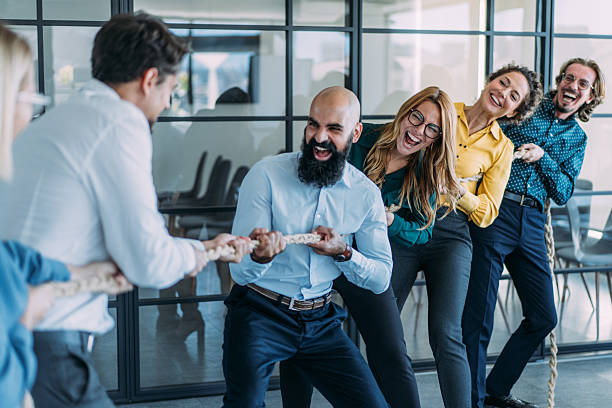 istock Playful colleagues having fun while playing tug-of-war in the office. 2246155505