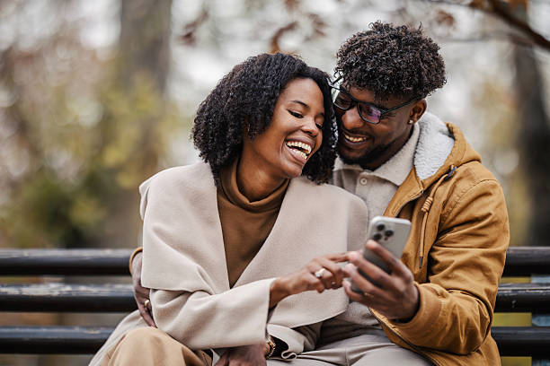 istock Happy black couple laughing viewing smartphone on park bench 2246155855