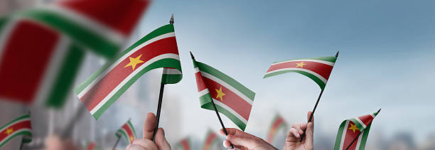 istock Suriname flags in their hands on a blurred urban background 2246168476