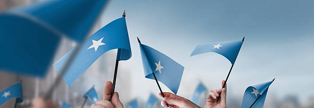 Somalia flags in their hands on a blurred urban background. The photo illustration was created without the use of artificial intelligence, only using Photoshop.