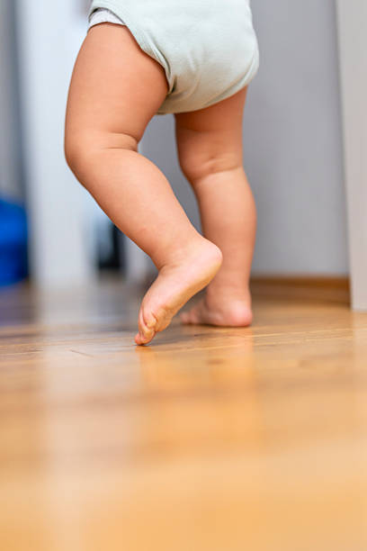 istock Curious Baby Taking First Steps on Wooden Floor Indoors with Bare Feet 2246171969
