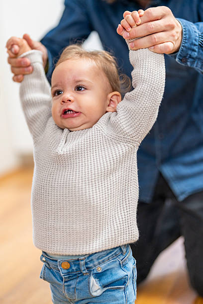 istock Joyful Caucasian Baby Taking First Steps with Father’s Support in Cozy Home Setting 2246171970