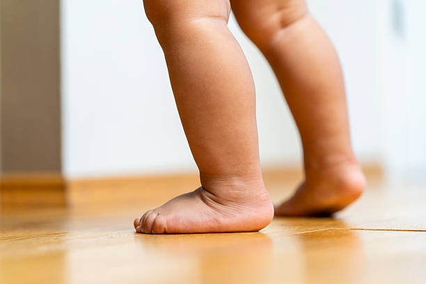 istock Curious Baby Taking First Steps on Wooden Floor Indoors with Bare Feet 2246172014