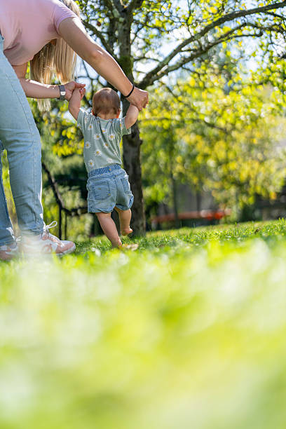 istock Joyful Young Caucasian Girl Taking First Steps with Mother's Support in Sunny Park 2246172122