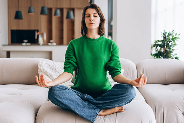 istock Woman meditating in lotus pose on couch at home 2246175621