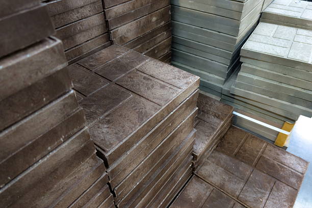 Sturdy concrete pavers are neatly stacked in a construction yard, showcasing various colors and textures under bright sunlight, ready for landscaping uses and outdoor projects.