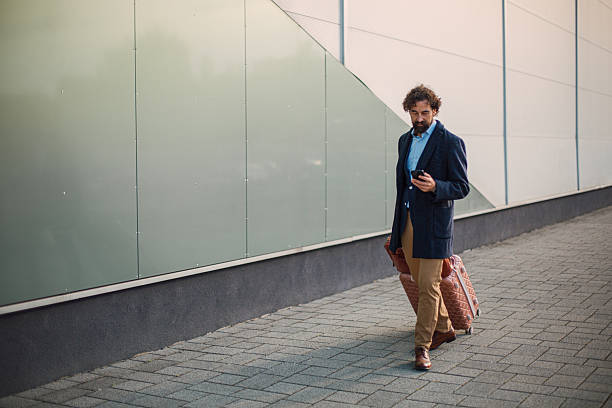 istock Businessman checking smartphone walking with luggage 2246179348