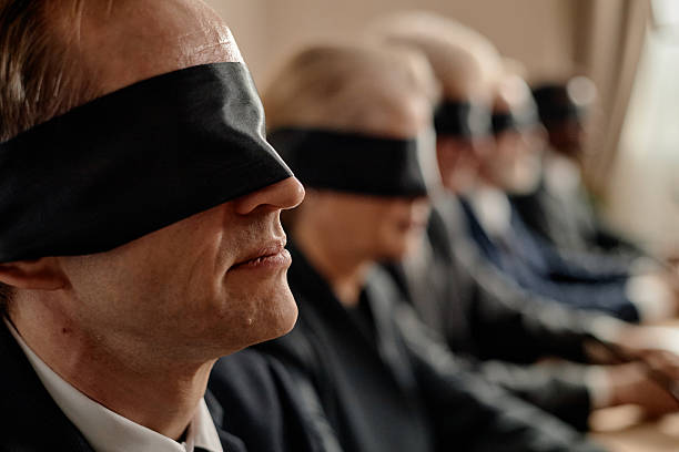 Row of middle aged and senior Caucasian and Black men and women sitting side by side wearing blindfolds, participating in group activity or training session indoors