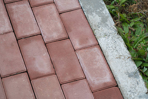 istock Red brick paving slabs next to concrete curb and green grass 2246192094