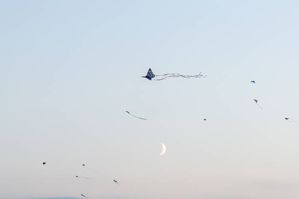 Berlin, Germany – September 27, 2025: Multiple colorful kites flying across the evening sky with the moon rising in the background during the Giant Kite Festival in Berlin.