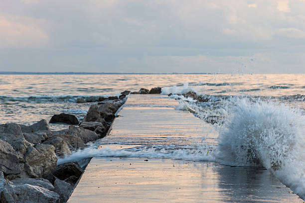 Dramatic waves crash against the stone pier in Grado, Italy, as the wind sweeps across the Adriatic Sea under a colorful evening sky — a vivid scene from the Northern Adriatic coast.
