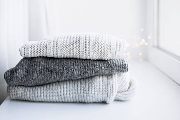 istock Stack of white and gray sweaters on windowsill with festive lights. 2246199150