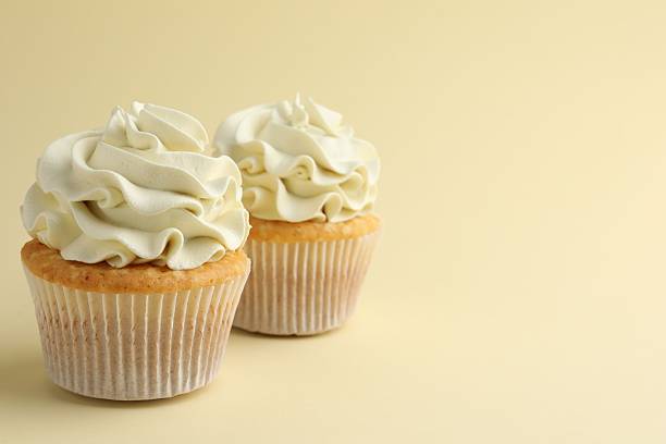 istock Tasty vanilla cupcakes with cream on pale yellow background, space for text 2246201162