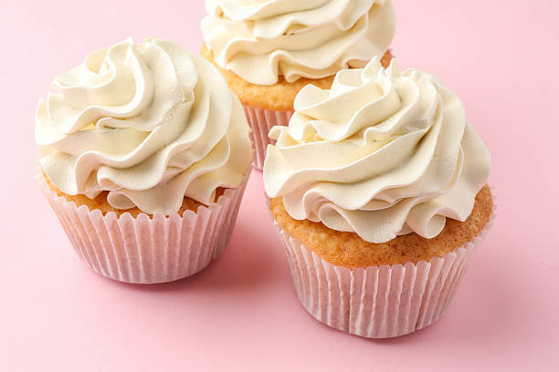istock Tasty vanilla cupcakes with cream on pink table, closeup 2246201259