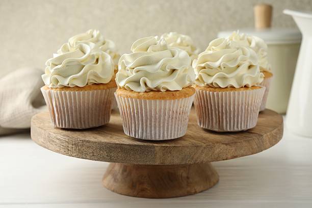 istock Tasty vanilla cupcakes with cream on white wooden table 2246201299