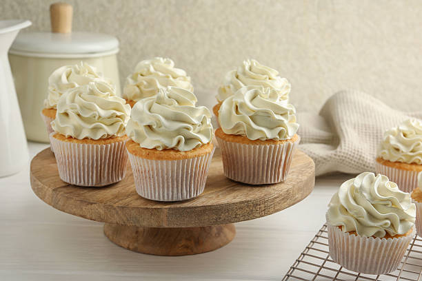 istock Tasty vanilla cupcakes with cream on white wooden table 2246201739