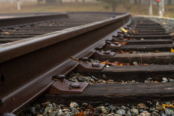 Rusty railway tracks curving through gravel and wooden ties on a foggy day