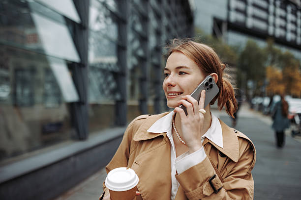istock Young well-dressed woman talking on smartphone while walking in city with coffee cup 2246203569