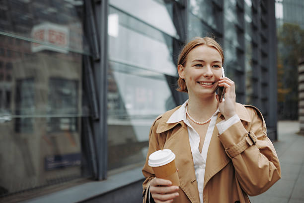 istock Young well-dressed woman talking on smartphone while walking in city with coffee cup 2246203580