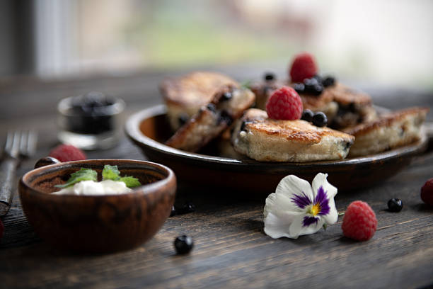 Homemade pancakes with fresh berries and cream served on wooden table, natural light breakfast still life.
