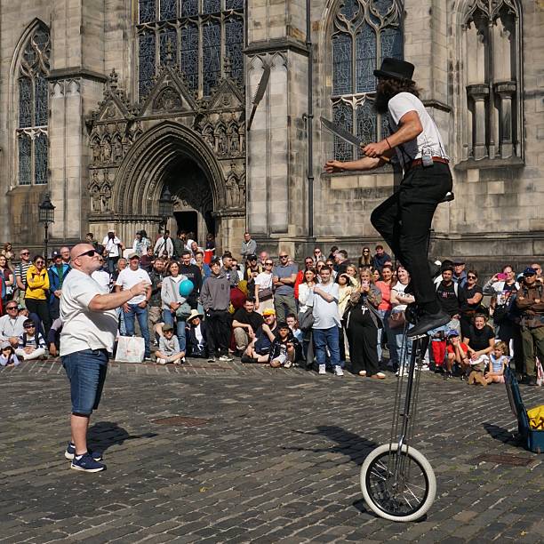 Edinburgh, Scotland - 18 August 2025: A juggler on a unicycle has attracted a large audience in front of St Giles Cathedral. A volunteer from the audience is throwing a knife to the performer.
