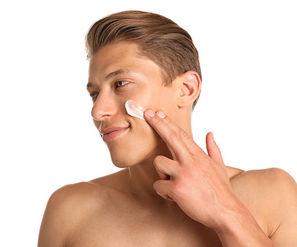istock Handsome young man applying cream onto his face on white background 2246217435
