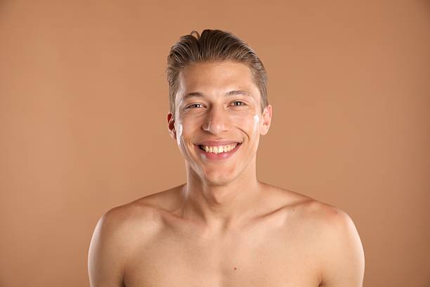 istock Handsome young man with cream on his face against light brown background 2246218747