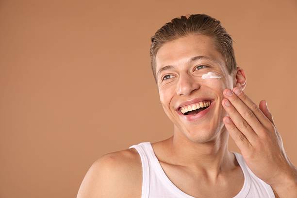 istock Handsome young man applying cream onto his face on light brown background, space for text 2246218832