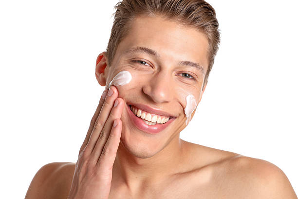 istock Handsome young man applying cream onto his face on white background, closeup 2246219202