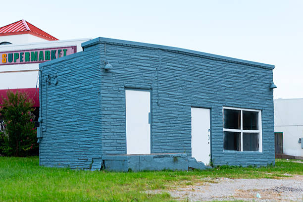 A uniquely small blue brick building with white doors and black windows sitting on very green grass.