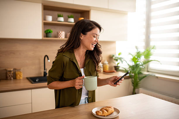 istock Happy woman browsing phone during breakfast in kitchen 2246225209