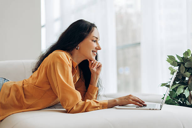 istock Smiling middle aged woman using laptop, freelancer working at home, lying on comfortable sofa 2246225403