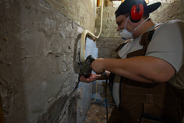 istock A worker prepares for a renovation, using a hammer drill to remove old plaster and cement from a wall wearing protective ear protection and a respirator mask Removing old plaster with a hammer drill. 2246225855