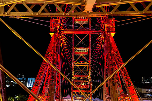 A brightly lit ferris wheel glows in vivid red hues against the night sky in Vienna, Austria. The urban skyline enhances the captivating nighttime atmosphere with a blend of modern and traditional architecture.