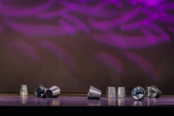 Latvian folk dance performance featuring traditional metal buckets arranged on stage, illuminated by vibrant purple lights, showcasing cultural artistry