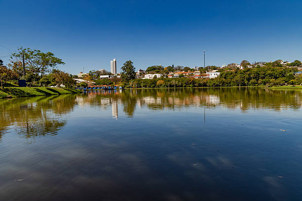 istock Tranquil Lake Reflecting Cityscape and Trees Under Clear Blue Sky 2246233628
