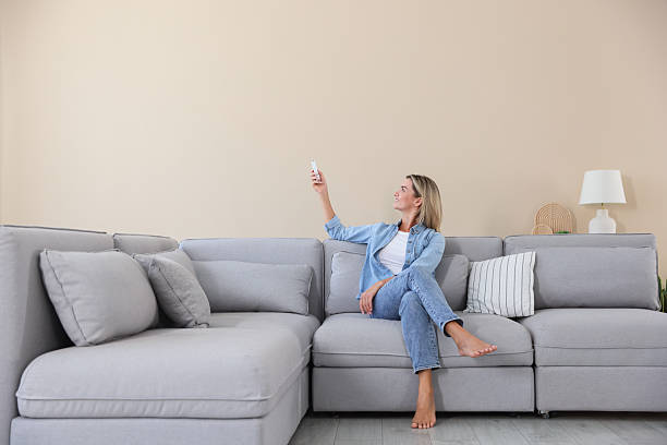 istock Woman using remote to control air conditioner on sofa at home 2246234324