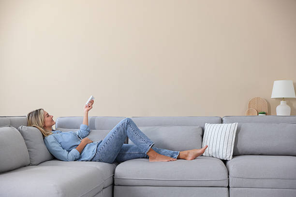 istock Woman using remote to control air conditioner on sofa at home 2246234344