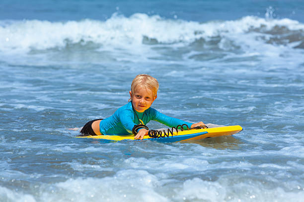 istock Happy young surfer boy with bodyboard have fun on beach, riding on small ocean waves. Summer adventures, active families, parents and kids lifestyle, sports activities on school holiday with kids 2246234748