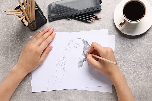 Woman drawing portrait sketch at grey table, top view