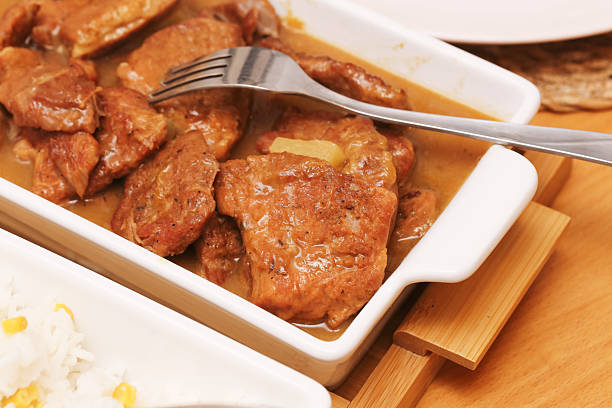 Homemade dinner concept with baked meat, rich gravy, and fork on wooden table. Tasty traditional meal closeup.