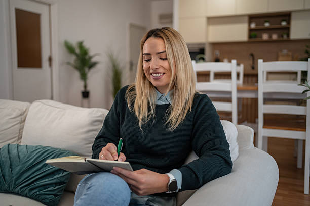 istock Young woman writing in journal on sofa at home 2246242494