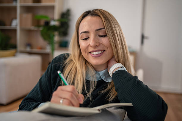 Young woman writing in diary, smiling, relaxing at home