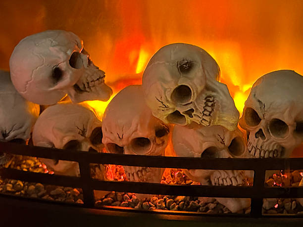 Stock photo shows a chilling Halloween scene featuring Halloween decorations on a cozy fireplace with a warm electric fire. Eerie skulls and spooky decorations create a haunting yet festive atmosphere