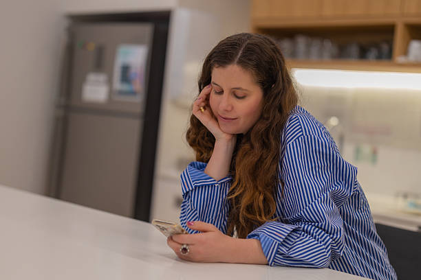 istock Young woman using smartphone at kitchen table in the morning 2246246710