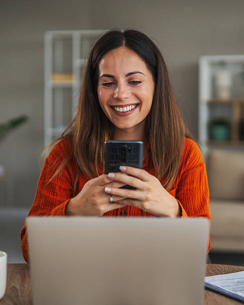 istock Woman smiling using smart phone and laptop working from home 2246253500