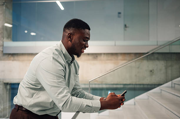 istock Young black man using smartphone on modern office stairs 2246253656